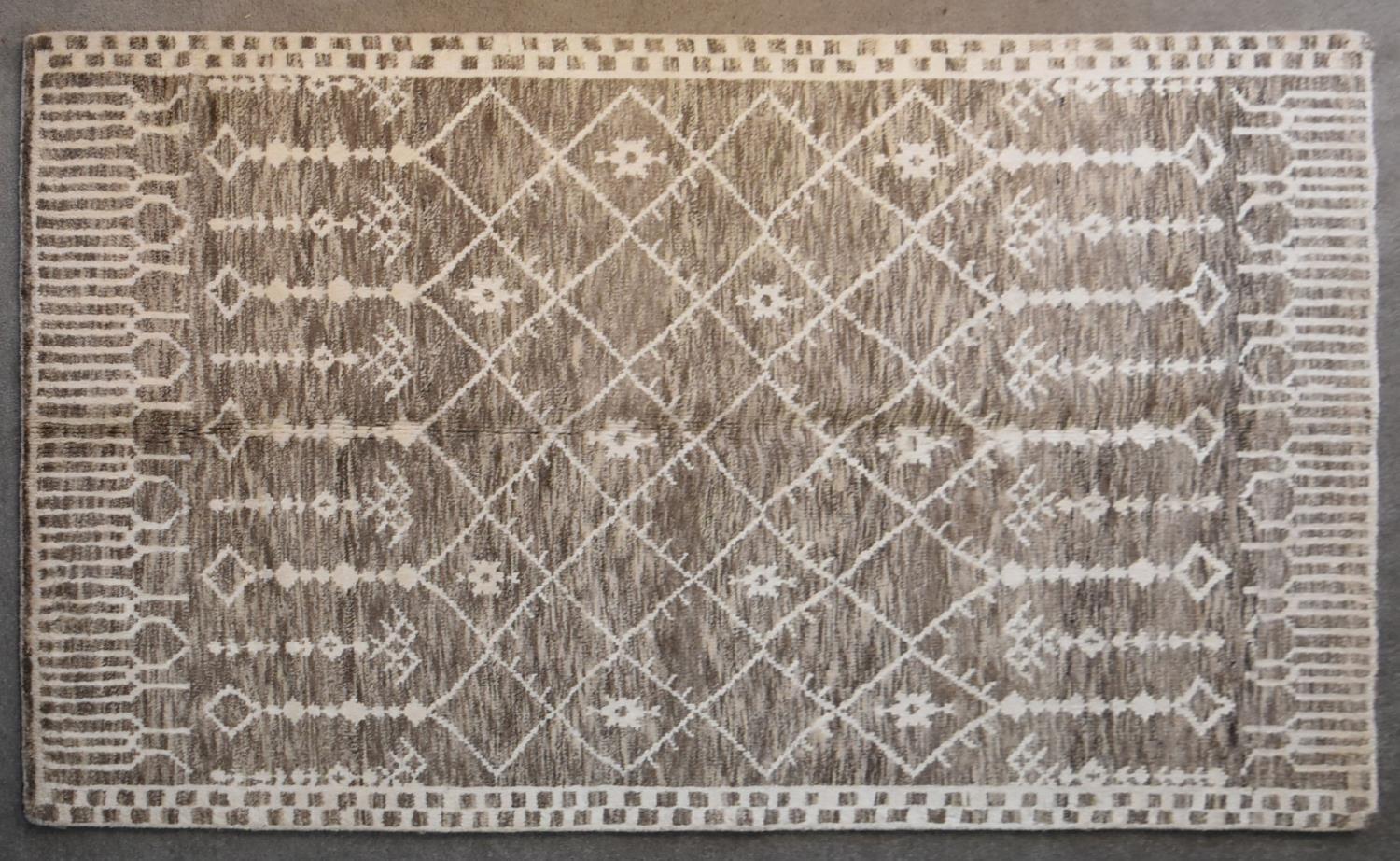 A Moroccan rug with repeating geometric, flowerhead and pendant design on a taupe ground. L.