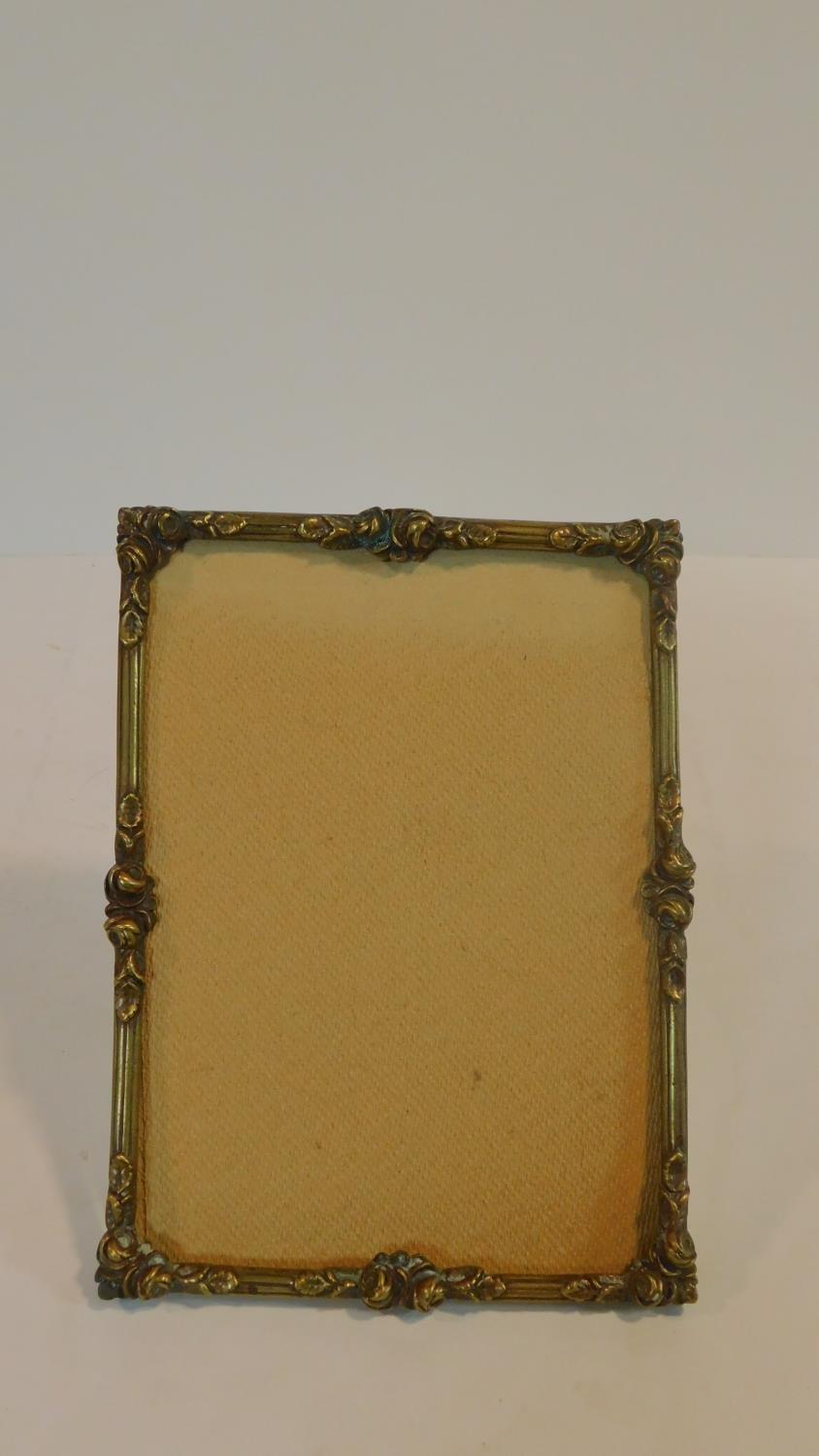 An antique brass relief moulded easel photo frame with roses and foliage and Y shaped brass hinged