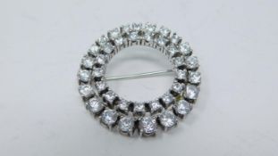 A white stone circular white metal brooch set with thirty eight round white paste stones in four