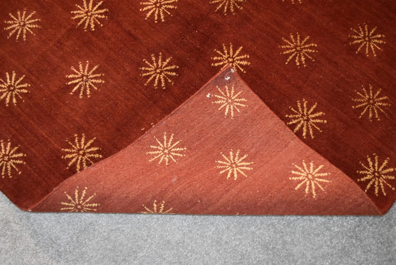 A silk and wool rug with repeating geometric flowerhead design on a burgundy field. L.237x170cm - Image 3 of 3
