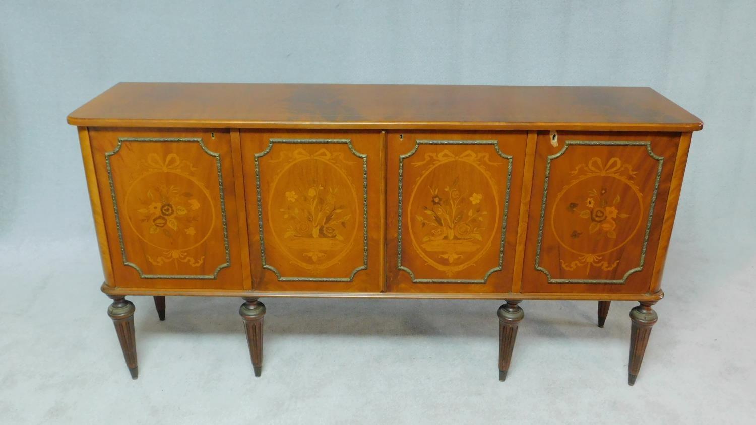 A Continental flame mahogany four door sideboard with floral inlaid panels on fluted tapering