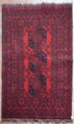 An Afghan rug with triple gul medallions on a deep red ground contained by stylised floral