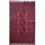 An Afghan rug with triple gul medallions on a deep red ground contained by stylised floral