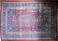 A Persian Mashad carpet with double central floral medallions on madder field within sapphire floral