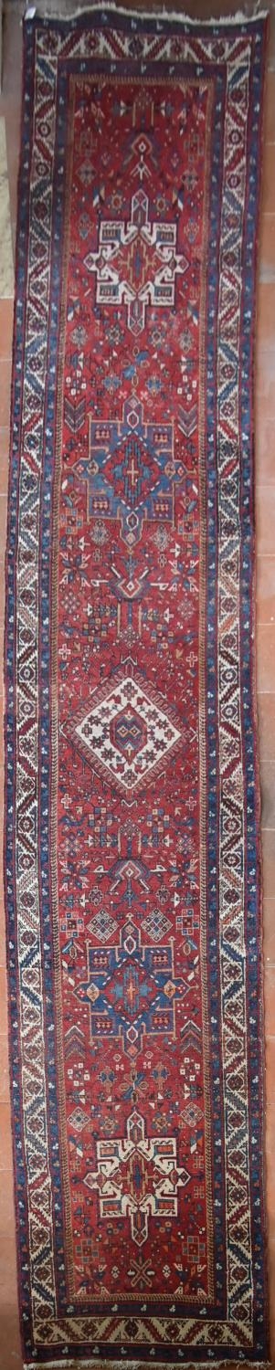An antique Persian Heriz runner with repeating star medallions on a madder ground enclosed by