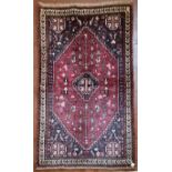 A Persian Kashkai rug with central stepped medallion and highly stylised motifs across a madder