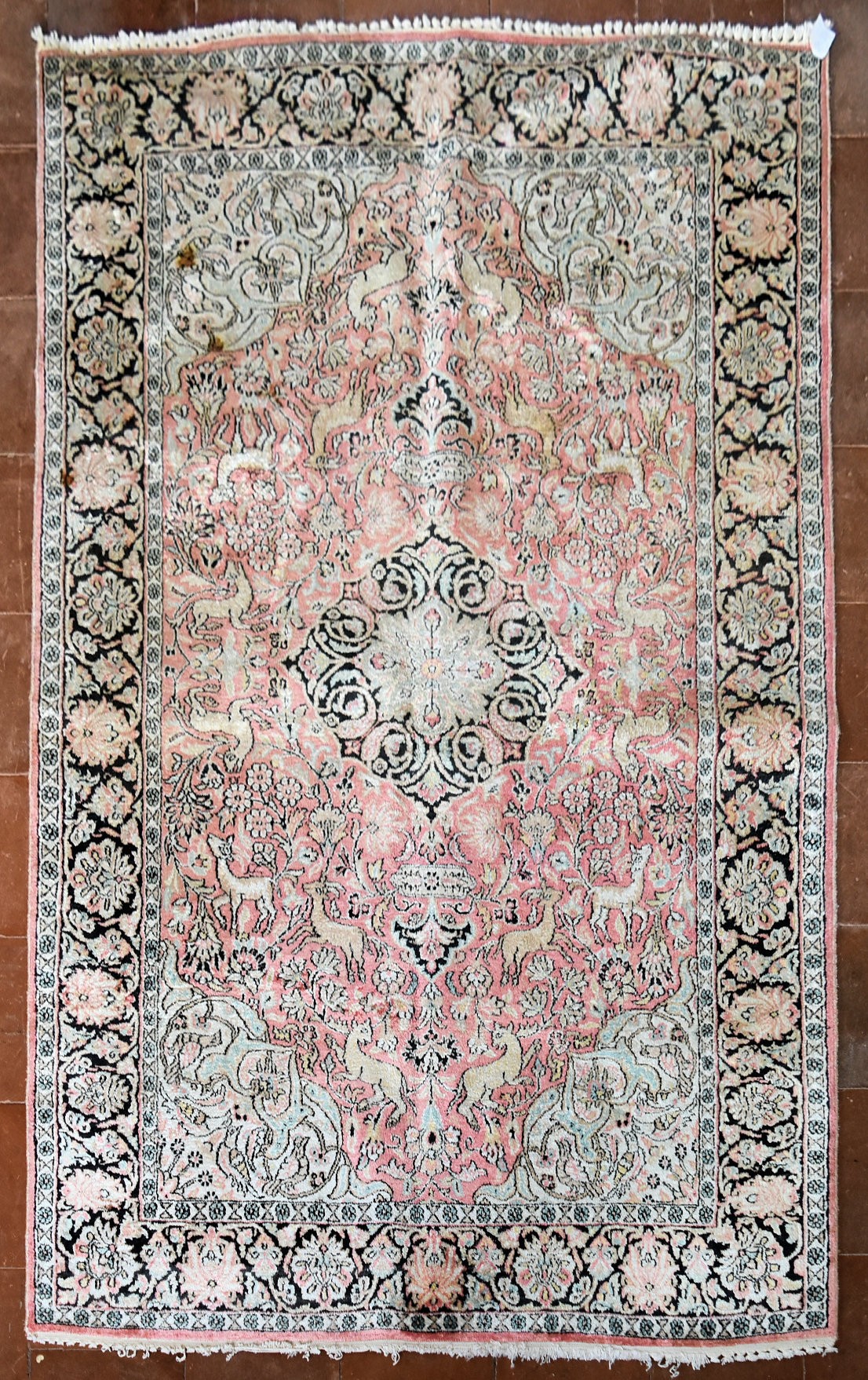 a Kashmir silk rug with floral medallion and spandrels on a salmon ground depicting animals in a