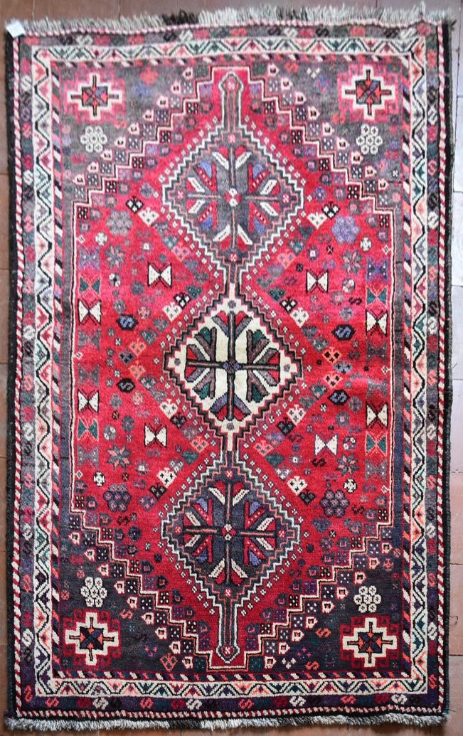 A Persian Shiraz rug with triple pole medallions on a madder ground contained by stylised floral