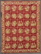 A hand made needlepoint carpet with repeating floral sprays across the brick red field contained