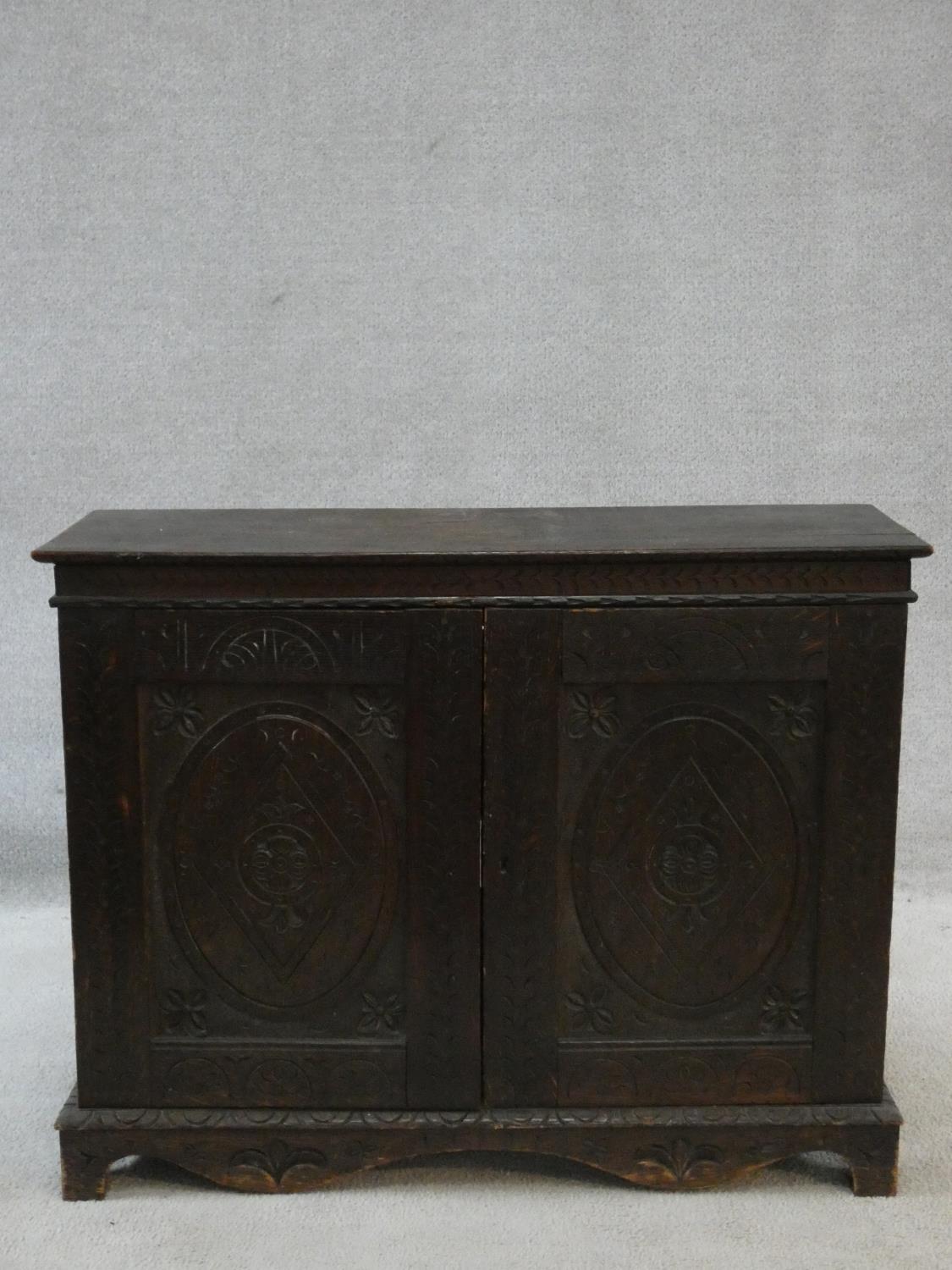 An antique country oak hall cupboard with a pair of carved panel doors on bracket feet. H.64 W.82