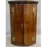 A Georgian mahogany bowfronted corner cabinet with dentil cornice above panel doors with original