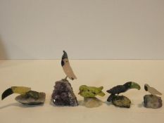 A collection of five carved bird figures from various gemstones standing on naturalistic quartz rock
