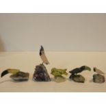 A collection of five carved bird figures from various gemstones standing on naturalistic quartz rock