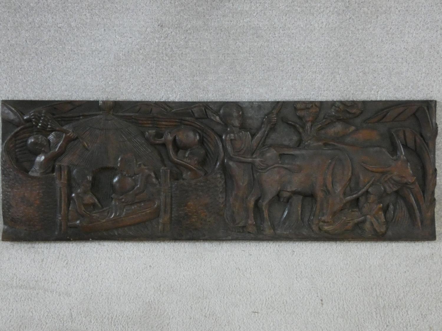 A carved African hardwood panel, farmers and cattle in a village setting, indistinctly signed to the