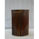 A Georgian mahogany bowfronted corner cabinet with oval fan satinwood inlay and a pair of fielded