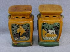 A pair of Chinese garden stools in ochre and sage green glaze with pierced decorative panels to each