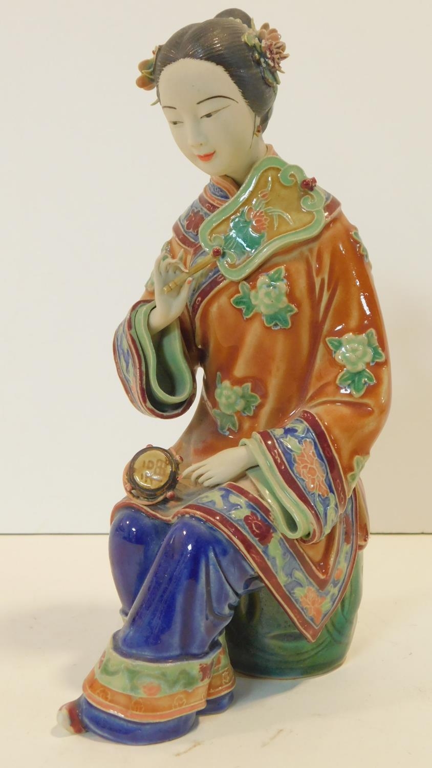 A Japanese ceramic figure of a lady sitting on a garden seat in polychrome hand painted decoration
