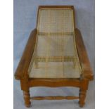 A Colonial style teak framed reclining planter's chair with caned back and seat and foldout foot