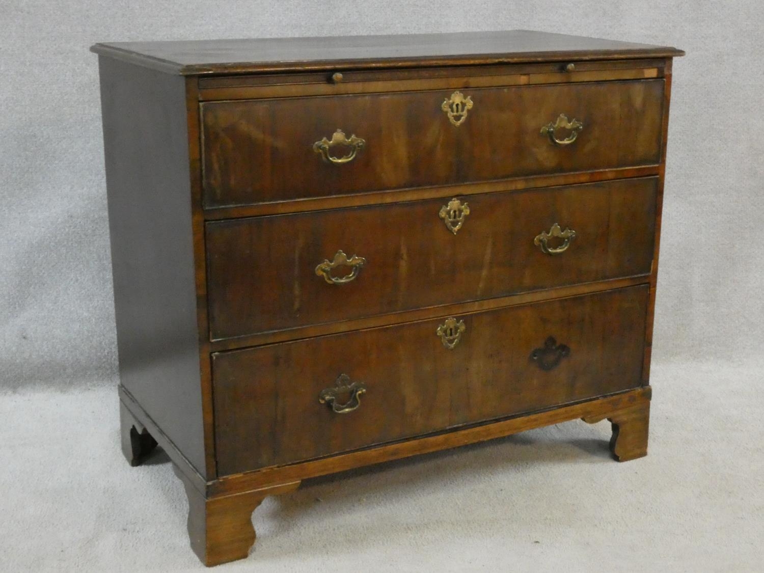 A Georgian walnut chest of three long drawers fitted with brushing slide raised on ogee bracket