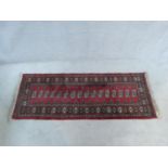 A Bokhara rug with repeating gul motifs on burgundy ground within stylised floral borders. 187x76cm