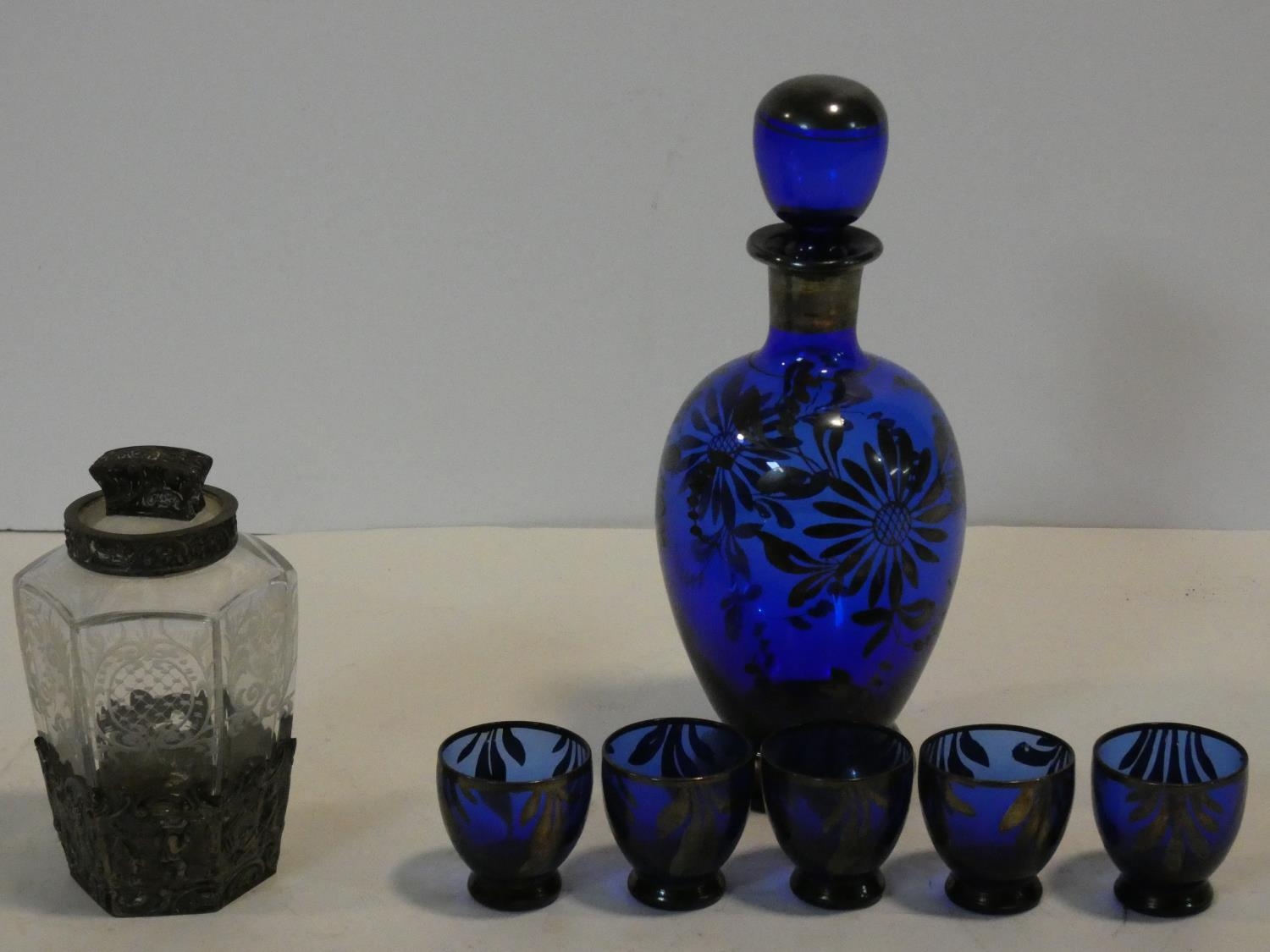 A cobalt blue glass decanter and shot glasses with painted silver floral design along with a