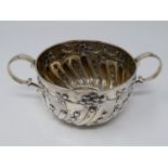 A two handled Victorian repousse design silver porriger with floral design and scrolling handles.