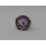 A 14ct gold and amethyst dress ring. Set with a round mixed cut amethyst in an open back four claw