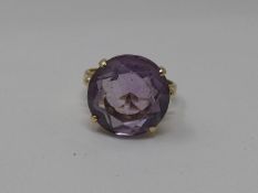 A 14ct gold and amethyst dress ring. Set with a round mixed cut amethyst in an open back four claw