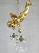 A ceiling chandelier in the form of a gilt putti supporting a pair of crystal drop light branches.