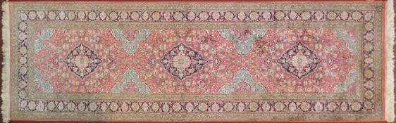 A Persian part silk runner with repeating triple medallions and scrolling floral decoration on a