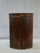 A Georgian mahogany bowfronted corner cabinet with oval fan satinwood inlay and a pair of fielded