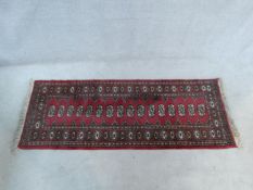 A Bokhara rug with repeating gul motifs on burgundy ground within stylised floral borders. 187x76cm