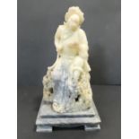 A large carved Eastern soapstone figure of a deity holding a sacred text perched on a rock raised on