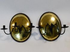 A pair of antique brass oval wall sconces with metal and brass riveted surrounds and wrought iron