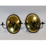 A pair of antique brass oval wall sconces with metal and brass riveted surrounds and wrought iron