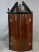 A Georgian mahogany bowfronted corner cabinet with broken architectural pediment above panel doors