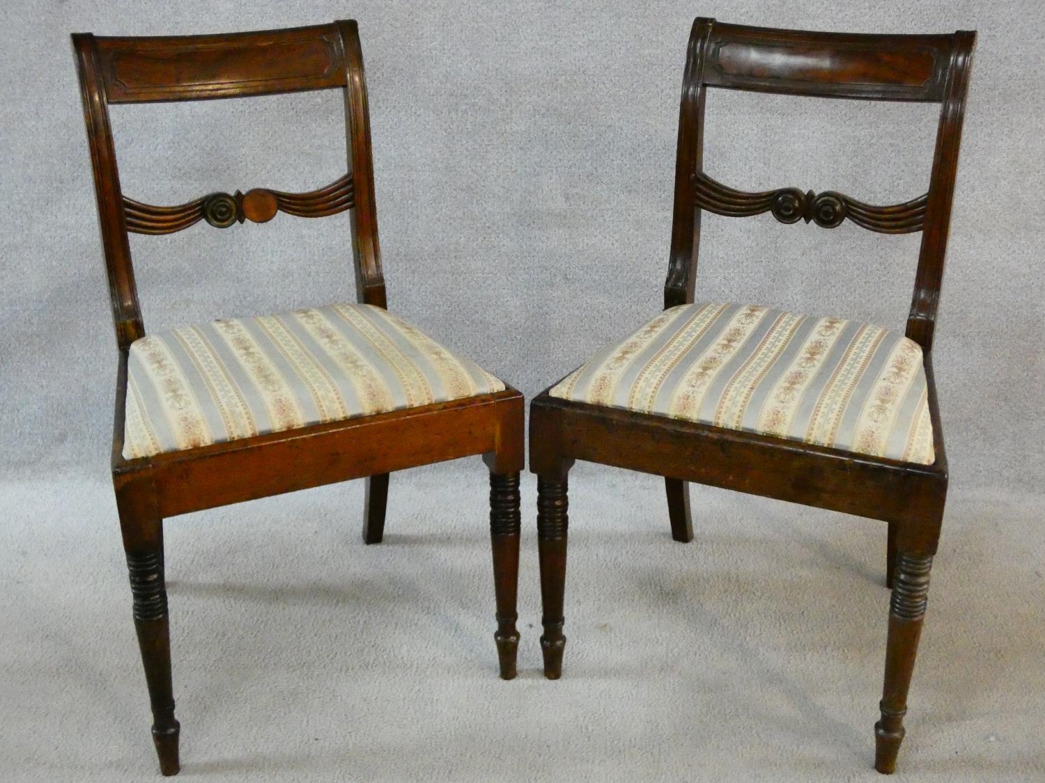A pair of late Georgian mahogany dining chairs with carved bar backs and splats above drop in