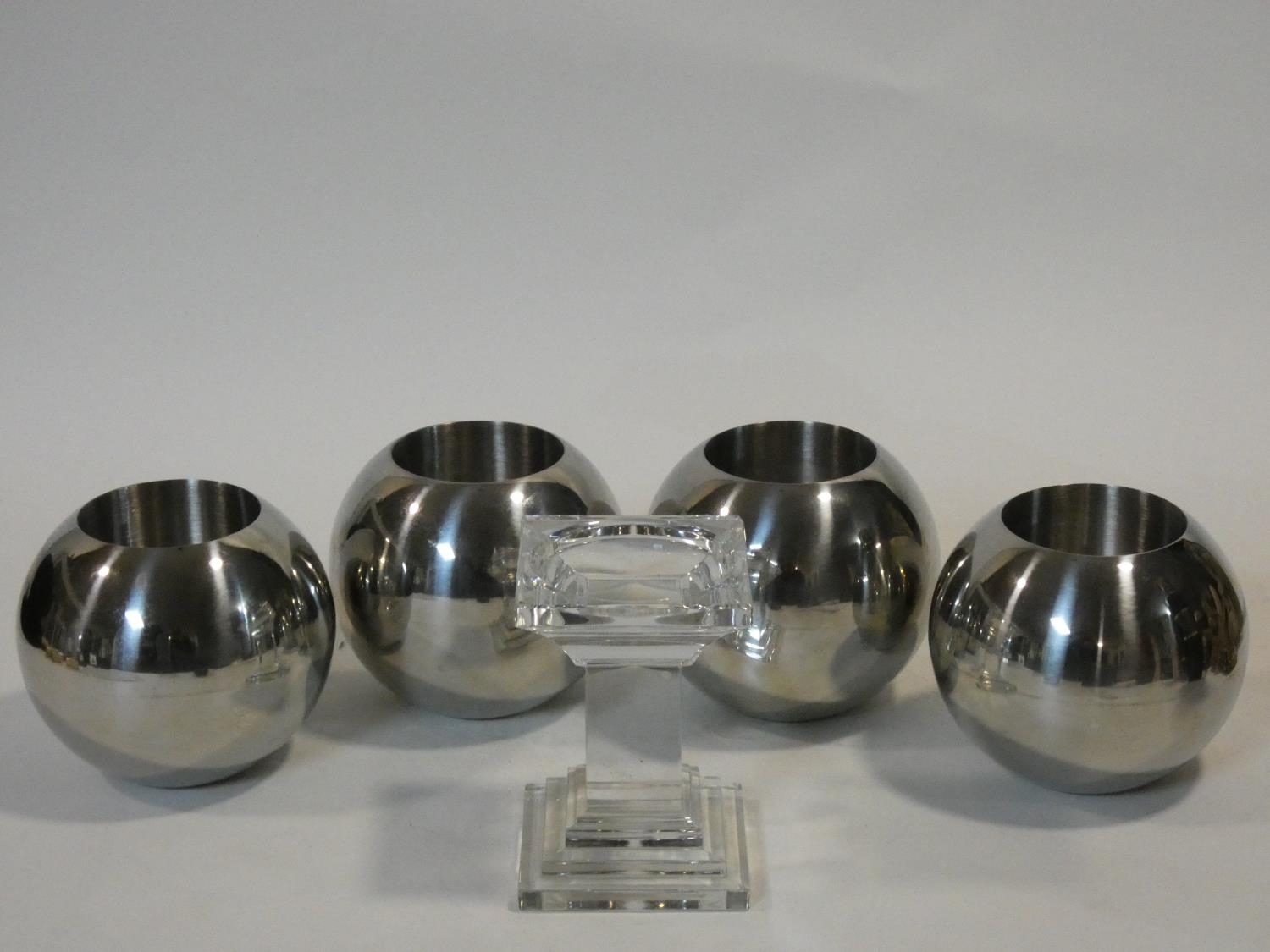 A set of four chrome spherical candle holders and a glass pedestal candle holder. H.14xW.10xL.10cm