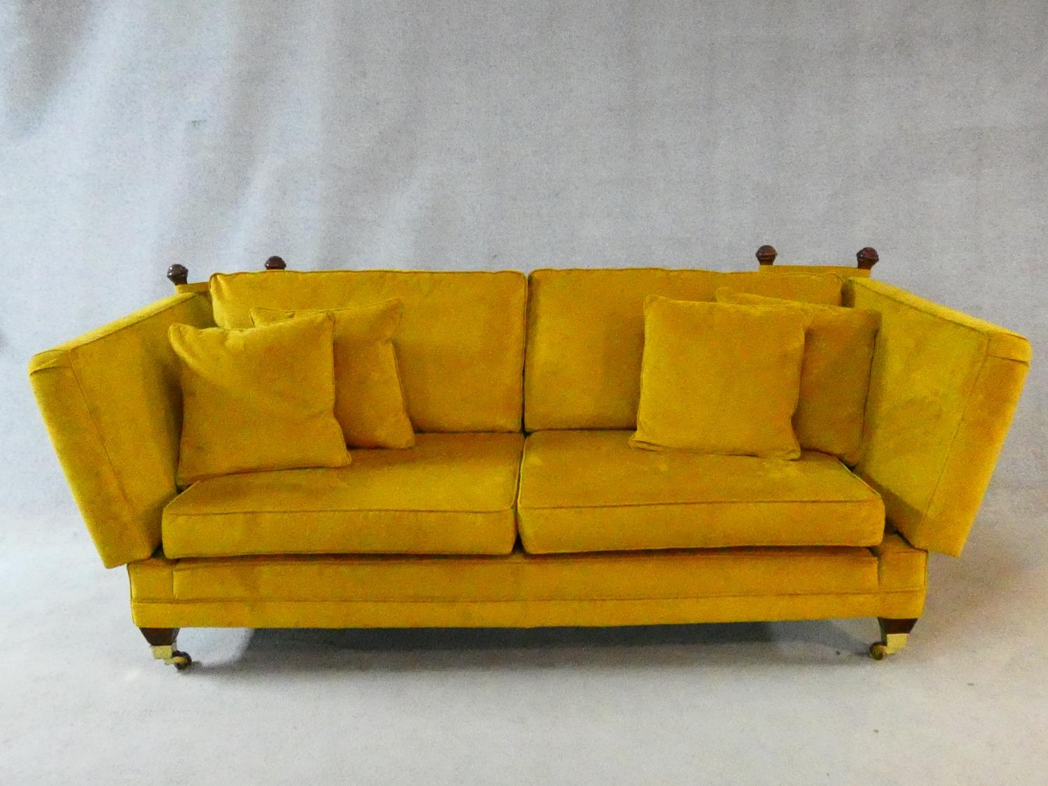 A contemporary Knole sofa in gold upholstery raised on squat square tapering supports on brass cup