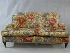 A Howard style sofa in floral upholstery on turned tapering supports terminating in brass and