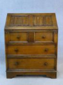 A mid century oak country antique style bureau with linen fold carving to the fall with fitted