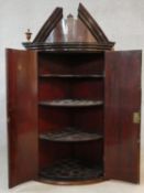 A Georgian mahogany bowfronted corner cabinet with broken architectural pediment above panel doors