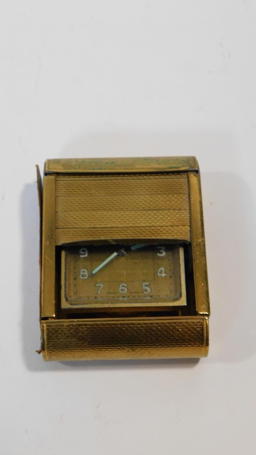 A gilt metal Swiss Made travel clock with engine turned decoration. Luminous numerals and hands.