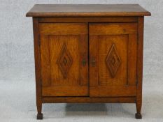 An early 20th century country oak style side cabinet with carved panel doors on squat square