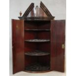A Georgian mahogany bowfronted corner cabinet with broken architectural pediment above panel doors