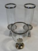 A pair of metal candle stands with glass storm shades and a similar single example with a flared