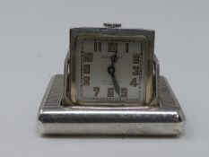 An Art Deco Dunhill silver miniature travel clock, the engine turned case with hinged divided