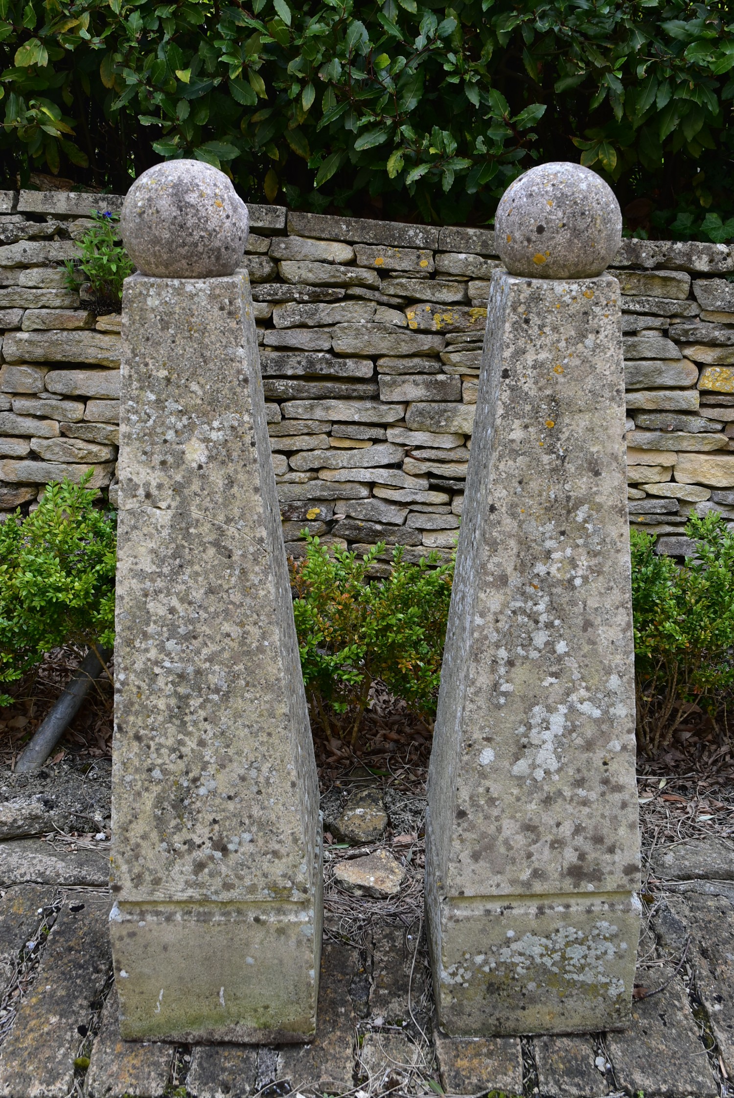 A pair of large weathered reconstituted stone garden obelisks topped with removable spheres. H.132cm