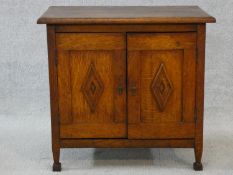 An early 20th century Arts and Crafts oak side cabinet with carved panel doors on squat square