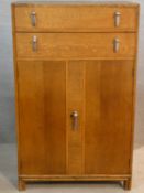 A mid century oak Art Deco style tallboy cabinet with two drawers above panel doors fitted with